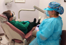 Dentist in PPE attends to a pediatric patient in exam chair