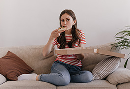 Young woman eating pizza straight from the box on her couch