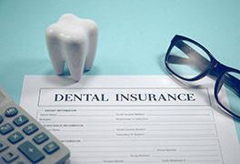 Dental insurance form with eyeglasses, calculator and a large replica tooth