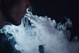 Close-up of a young man exhaling a cloud of smoke using an electronic cigarette